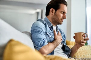 young man feeling sick holding his chest pain while drinking tea living room
